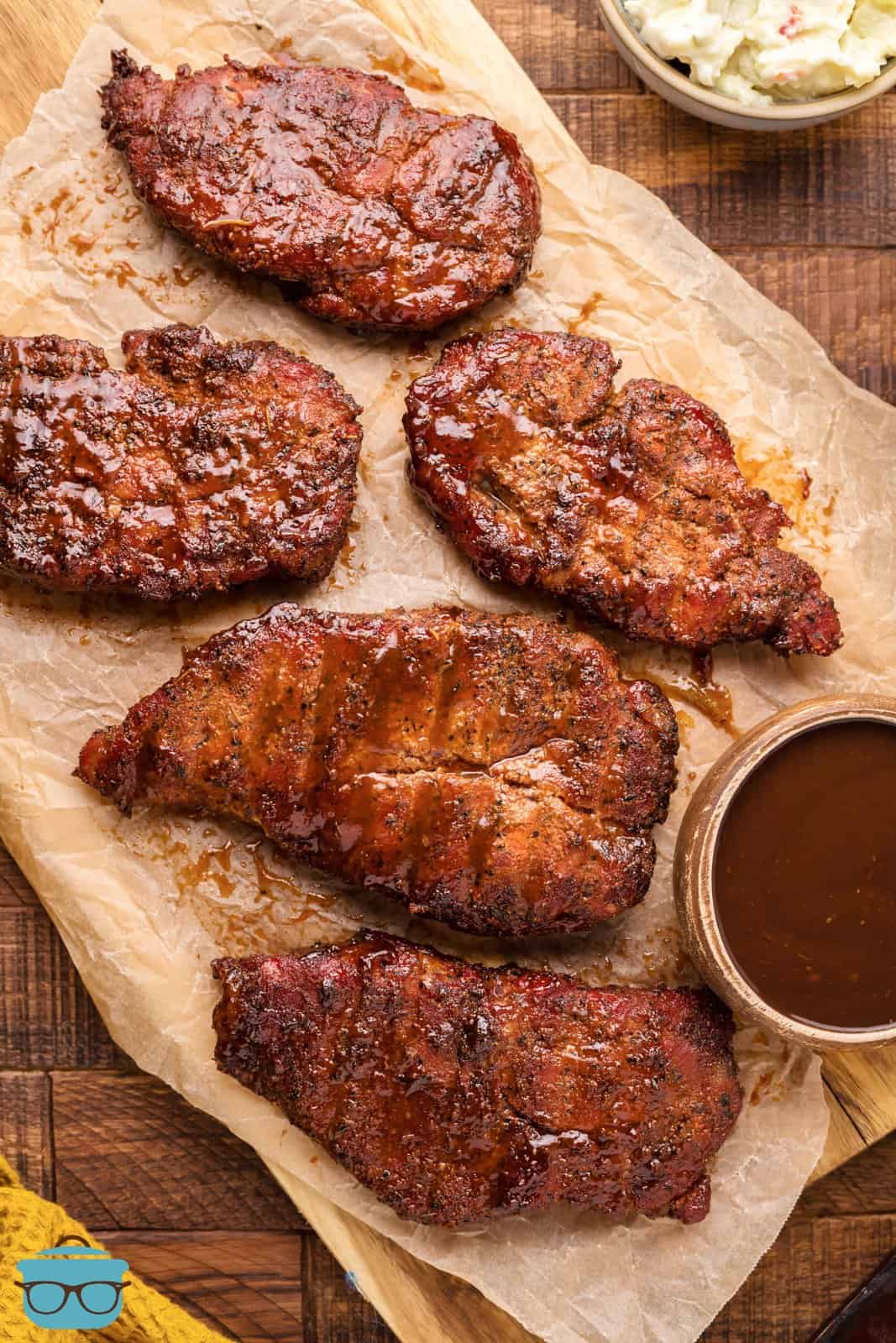Smoked Pork Steaks overhead on butcher paper with BBQ sauce on side.