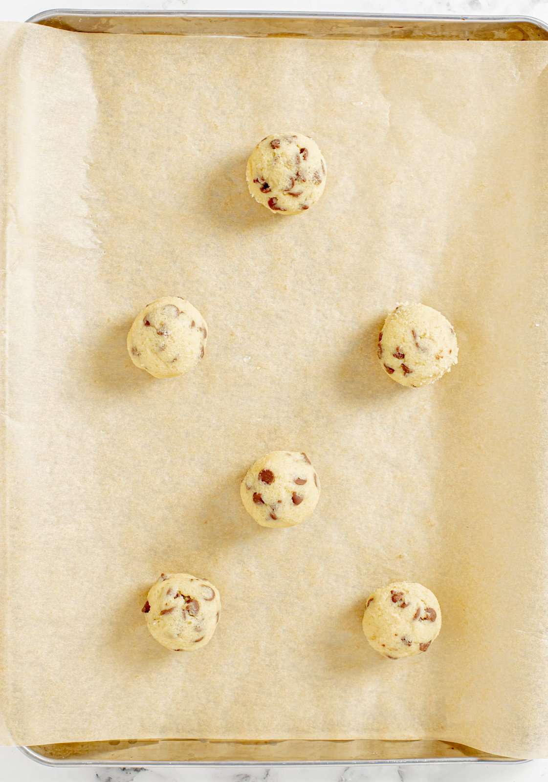 Cookie dough balls rolled out on parchment lined baking sheet.