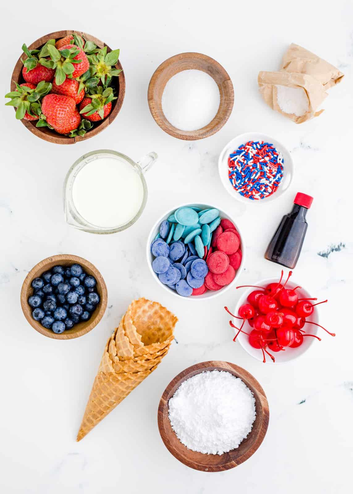 Ingredients needed: waffle cones, red melting candies, blue melting candies, strawberries, blueberries, granulated sugar, heavy cream, powdered sugar, cheesecake pudding mix, vanilla extract, maraschino cherries, red, white and blue sprinkles.
