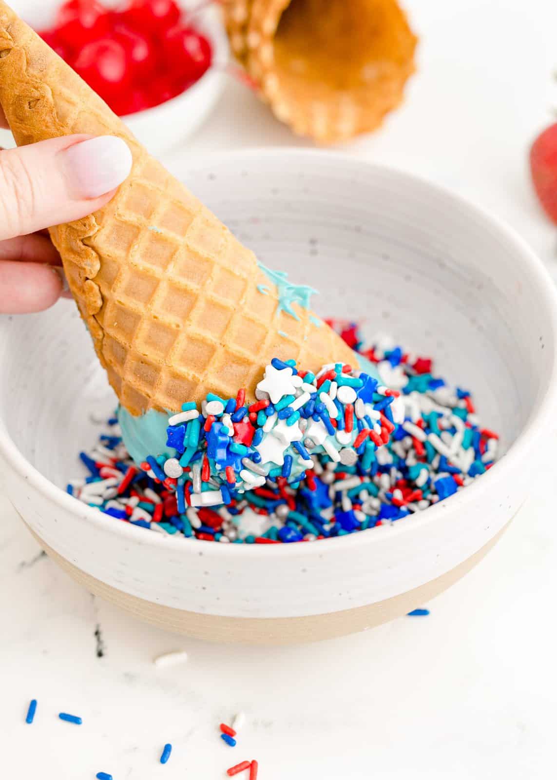 Waffle cone being dipped into sprinkles.