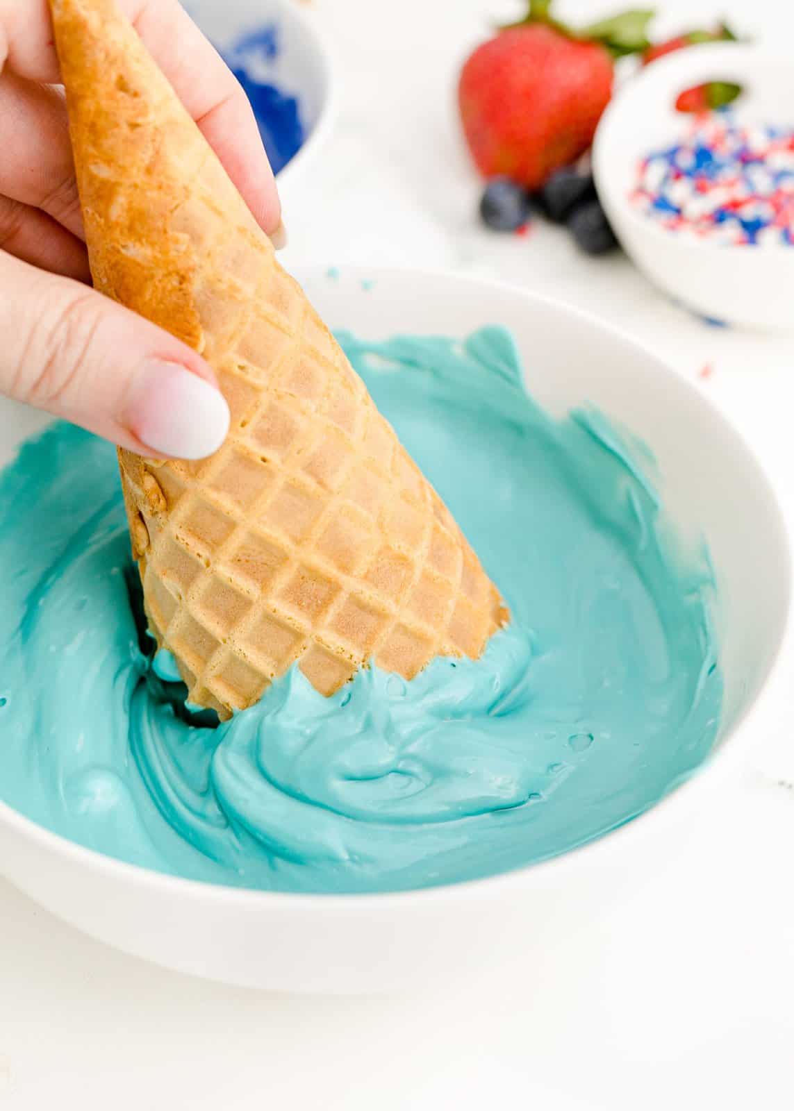 Waffle cone being dipped into candy melts.