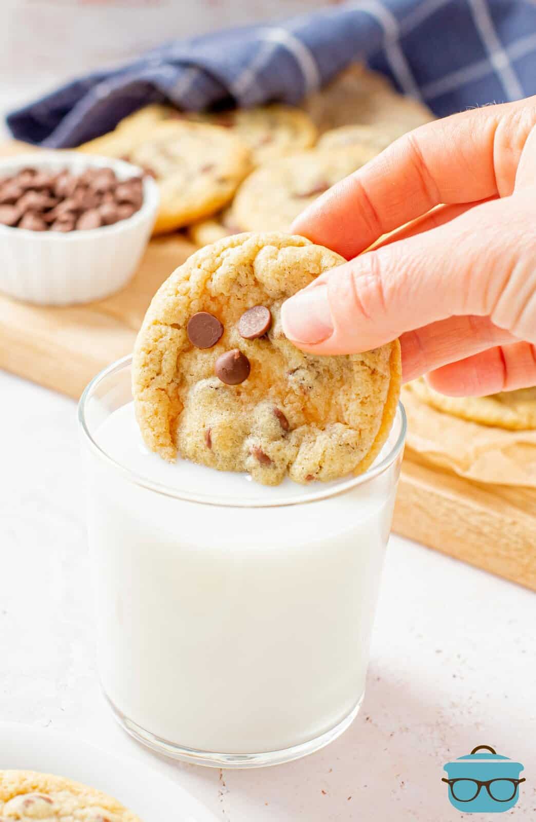 Hand dipping one Chewy Chocolate Chip Cookie into milk.