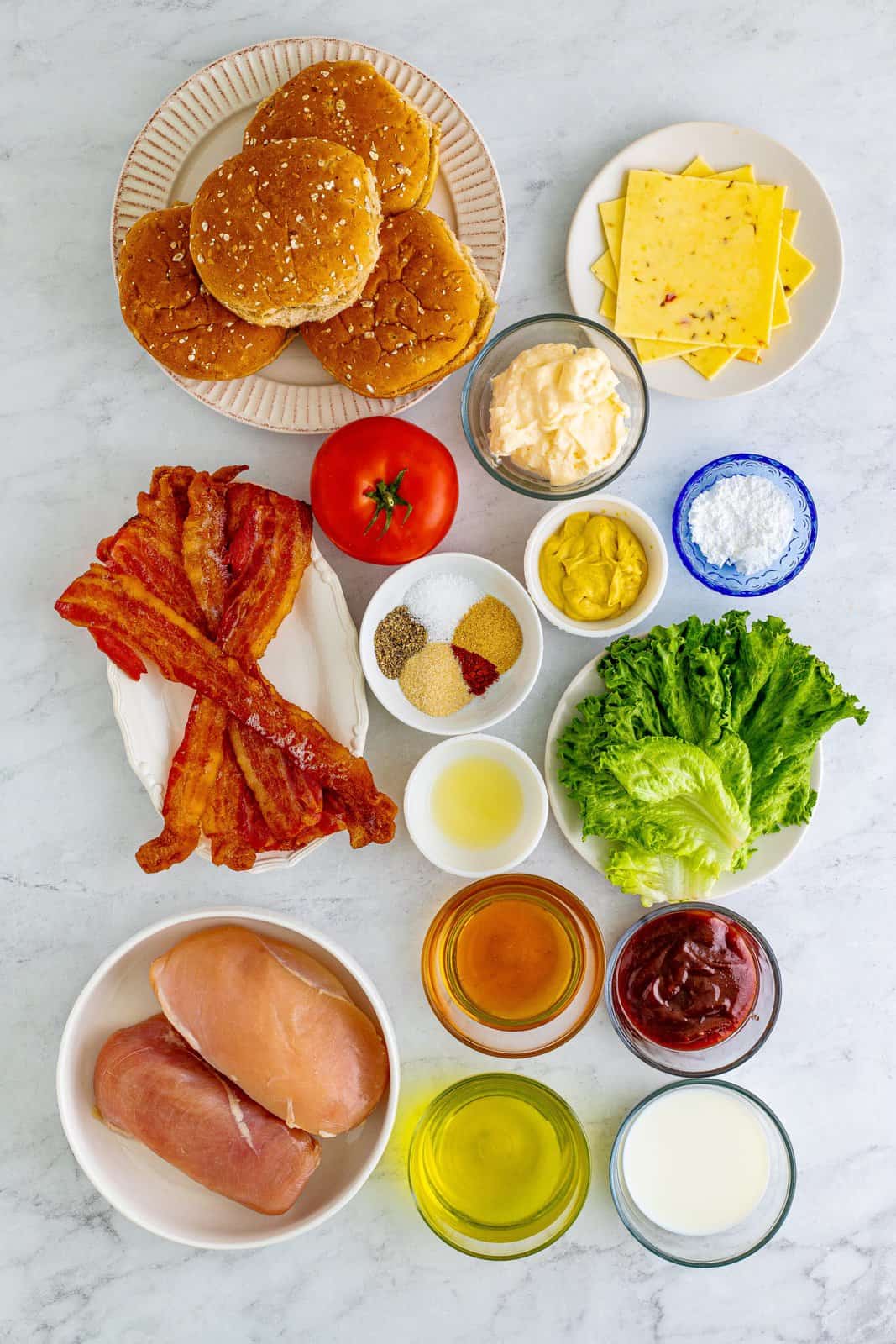 Ingredients needed: chicken breasts, dill pickle juice, whole milk, powdered sugar, garlic powder, onion powder, pepper, kosher salt, smoked paprika, mayonnaise, sweet bbq sauce, honey, dijon mustard, lemon juice, pepper jack or colby jack cheese, multigrain buns, green leaf lettuce, beefsteak tomato slices and applewood smoked bacon.