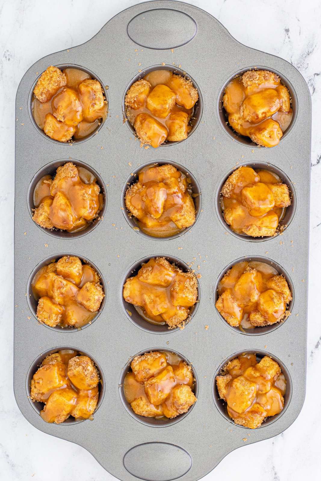 Sauce drizzled over cinnamon roll pieces in muffin tin.