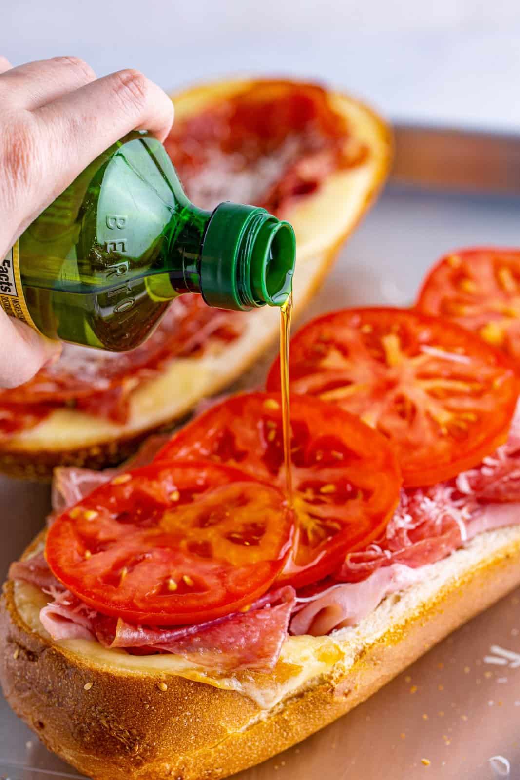 drizzling olive oil over sliced tomatoes on a sub roll.