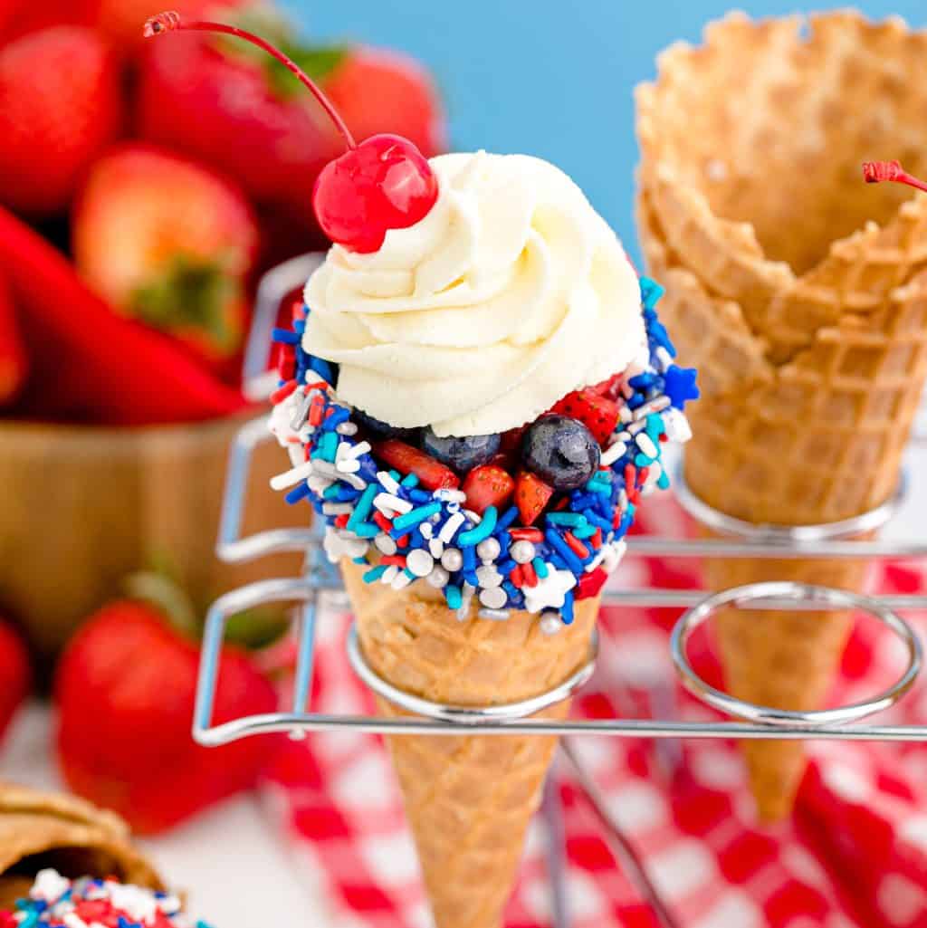 Square image of finished 4th of July Waffle Cones in cone holder topped with cherry.