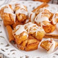 Square image of Cinnamon Roll Monkey Bread Muffins on white plate with bite removed covered in glaze.