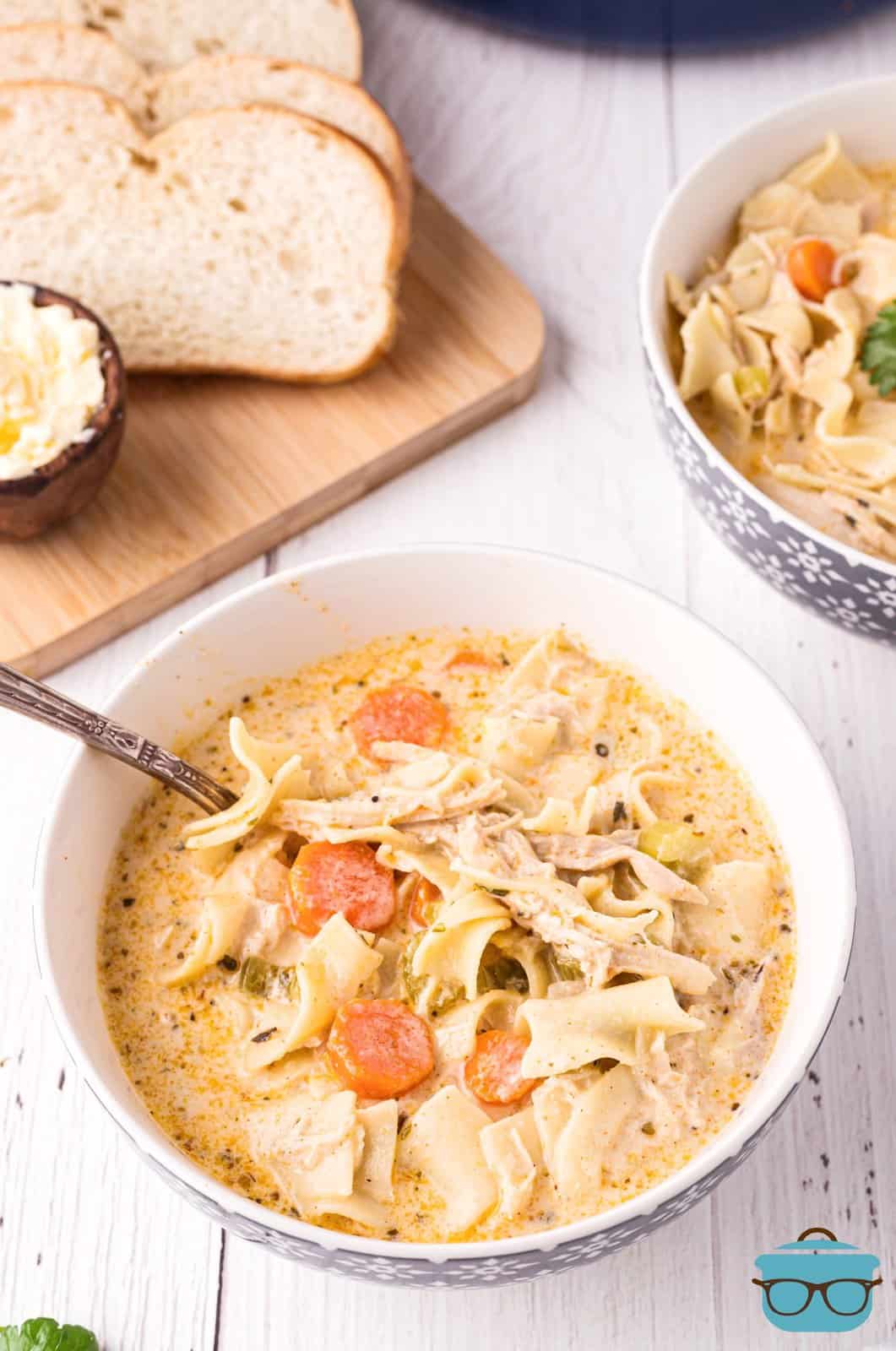 Creamy Chicken Noodle Soup in bowl with spoon and bread in background.