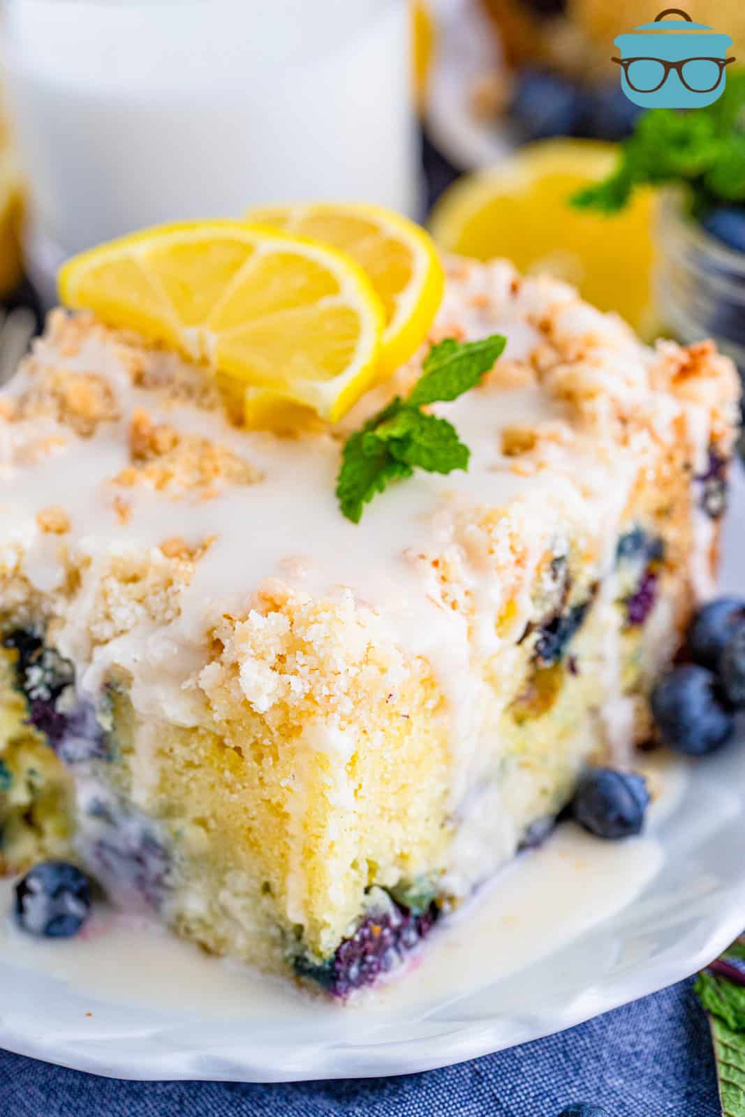 Slice of Lemon Blueberry Coffee Cake on plate topped with glaze, lemon slices and mint.
