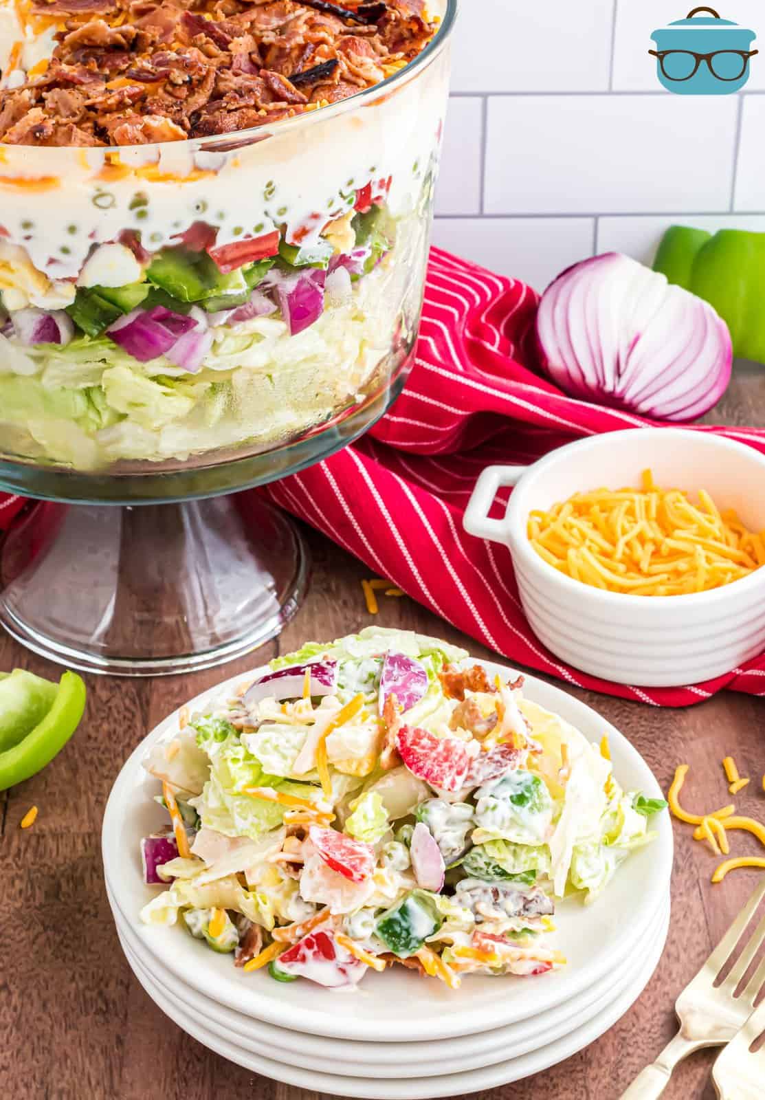 Seven Layer Salad scooped onto white plate with bowl of salad in background.