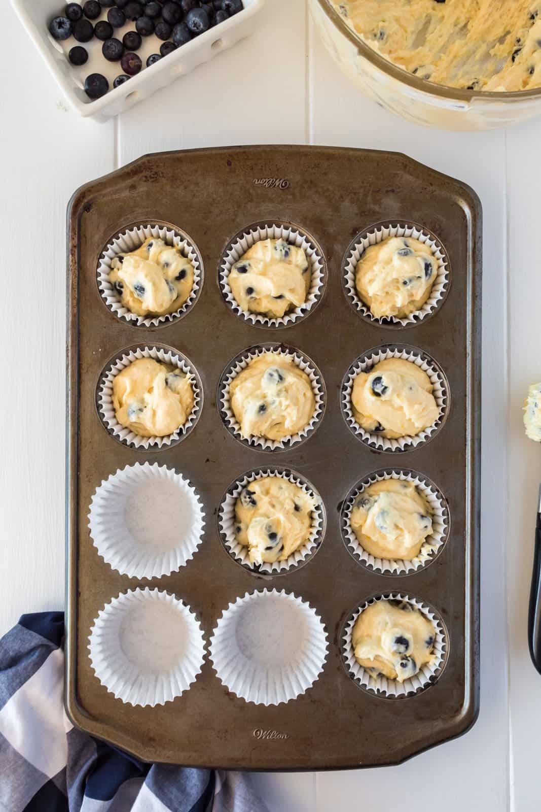Muffin batter added to paper cups in muffin tin.