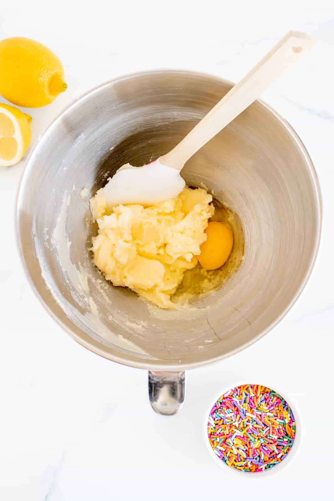 Burro e zucchero sbattuti nella ciotola della planetaria con l'aggiunta di uovo insieme all'estratto di mandorle, panna acida e succo di limone.