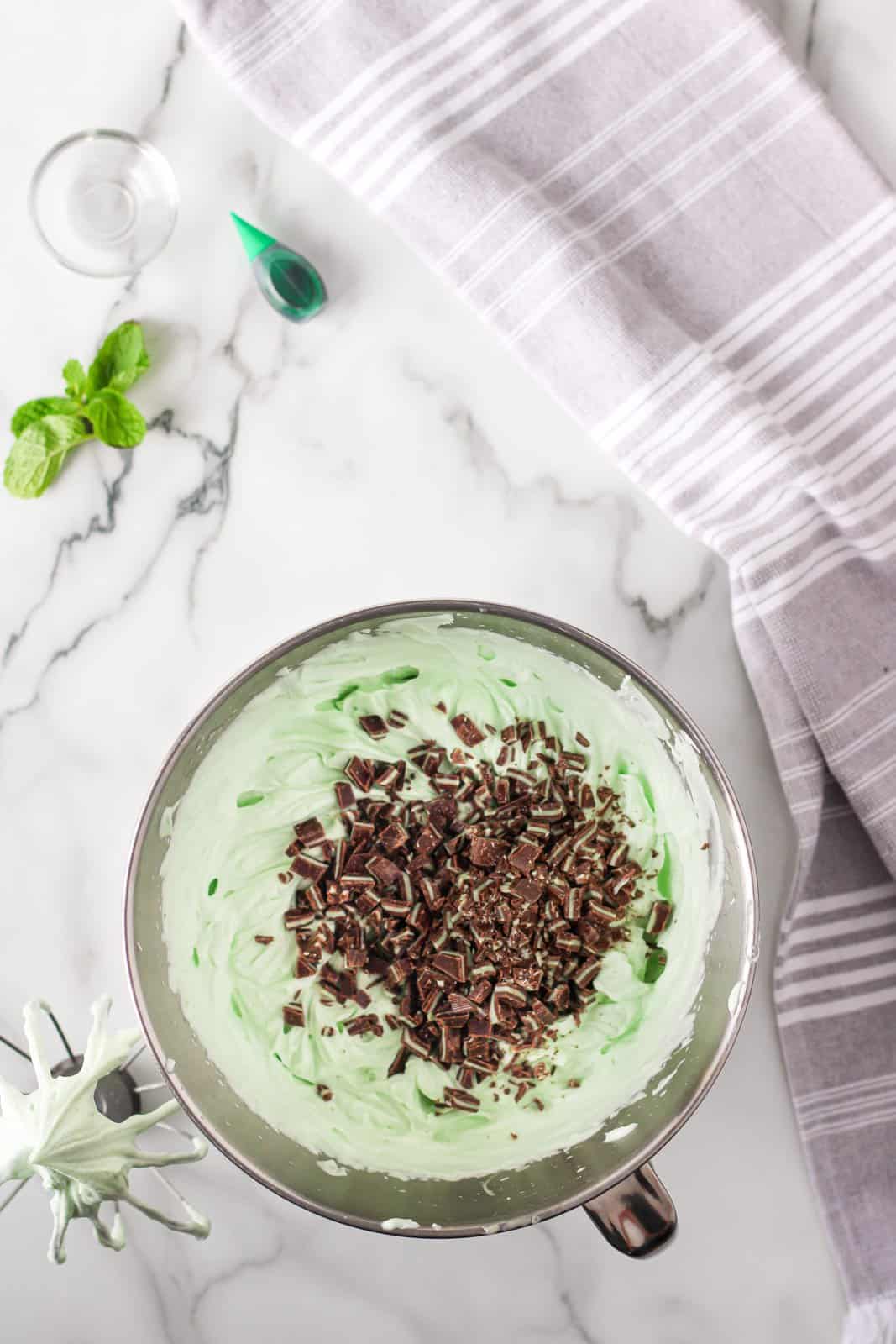 Mint chocolate added to ice cream mixer in bowl of stand mixer.