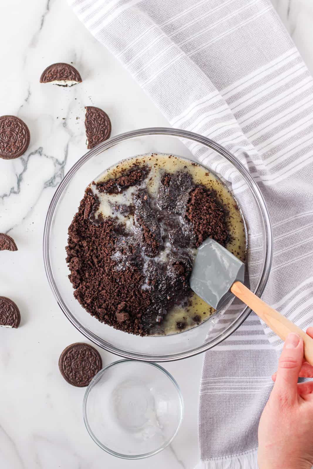 Oreos being mixed together in bowl with melted butter.
