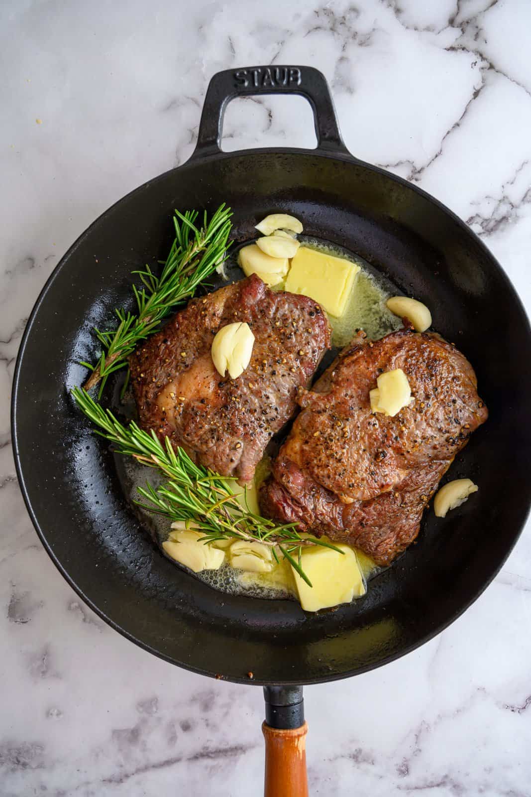 Steaks in pan with butter, garlic and rosemary sprigs.
