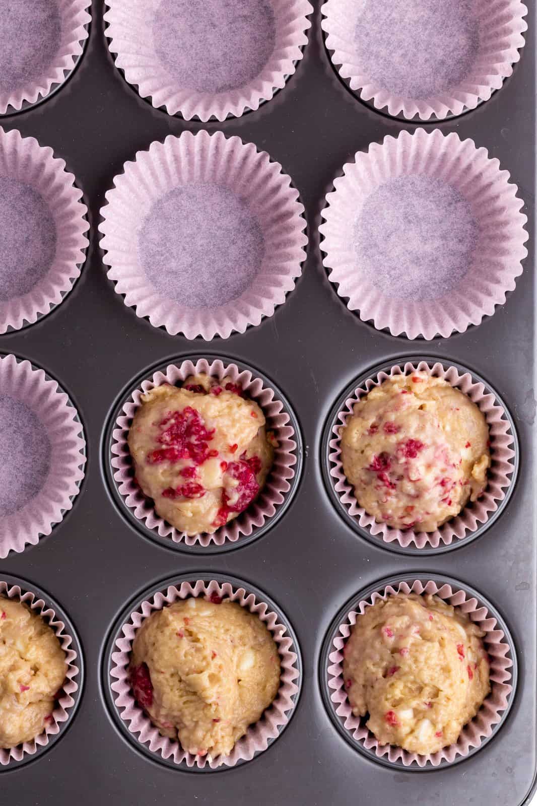 Muffin batter scooped into paper lined wells in muffin tin.