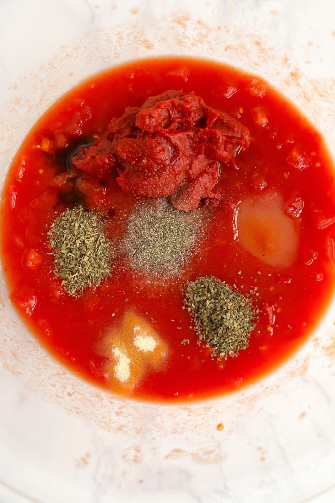 Tomatoes, tomato juice, tomato paste, sugar, worcestershire sauce, oregano, basil, garlic powder, salt, and pepper added to bowl.