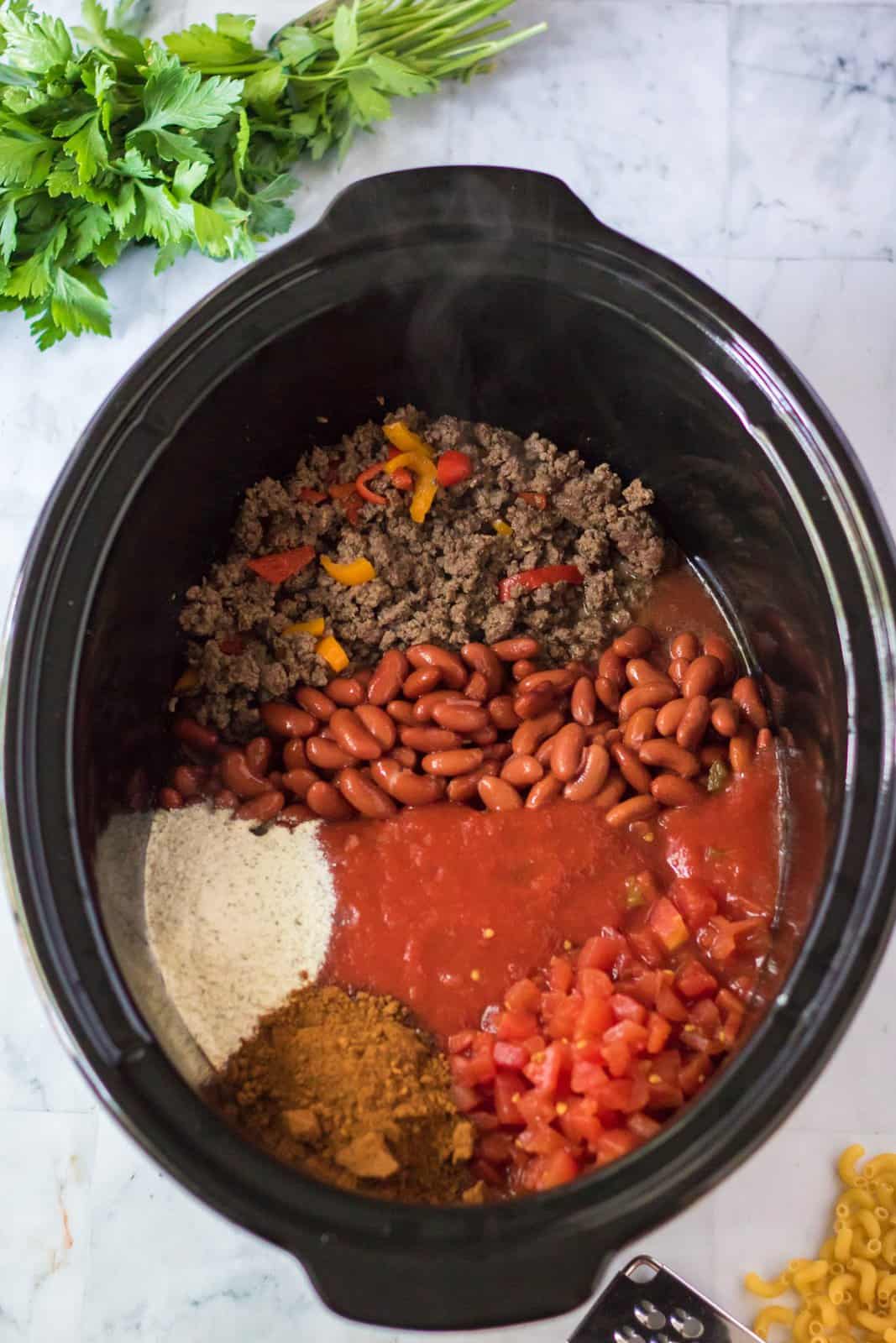 Browned beef, peppers, tomato sauce, rotel tomatoes, kidney beans, chili seasoning, ranch seasoning and water added to slow cooker.