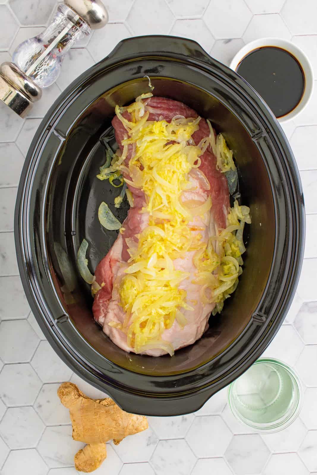 Pork loin in crock pot with sautéed onions on top.