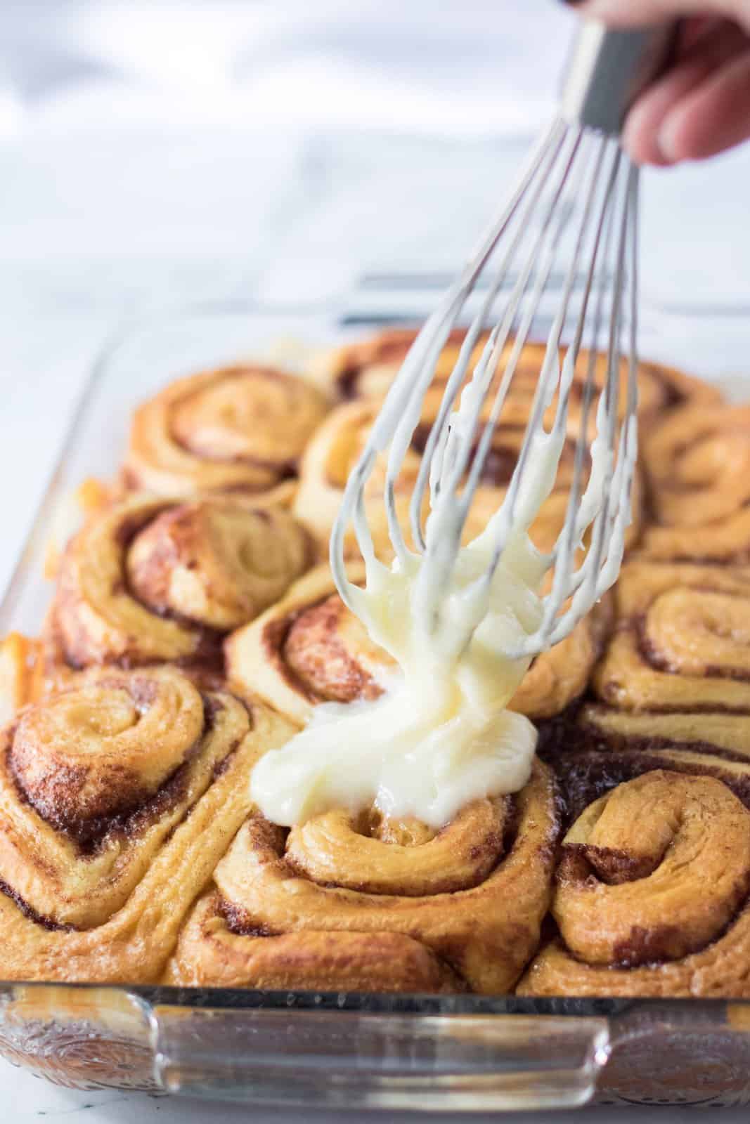 Icing being spread over baked cinnamon rolls.