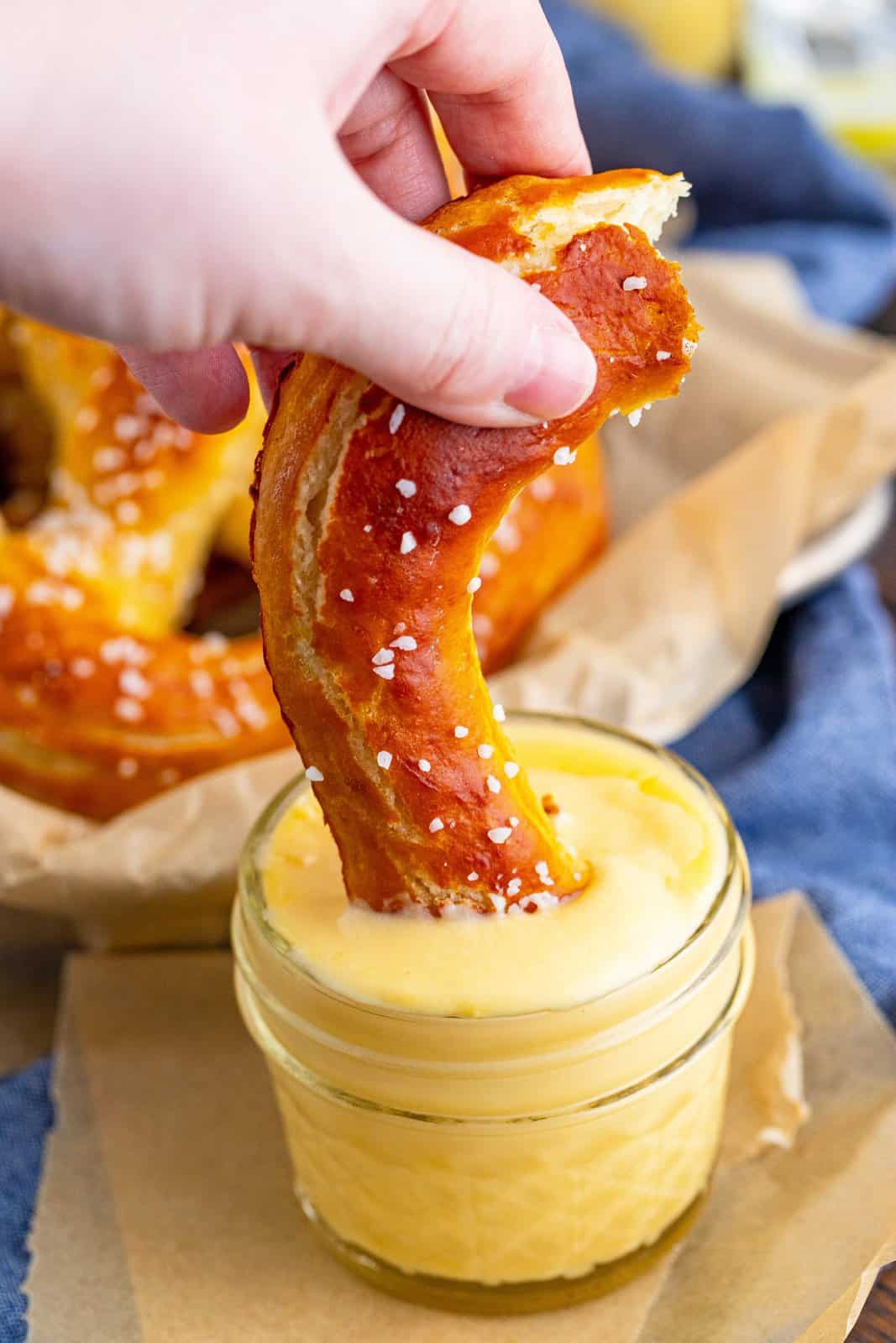 Hand dipping part of Homemade Soft Pretzels into cheese sauce.