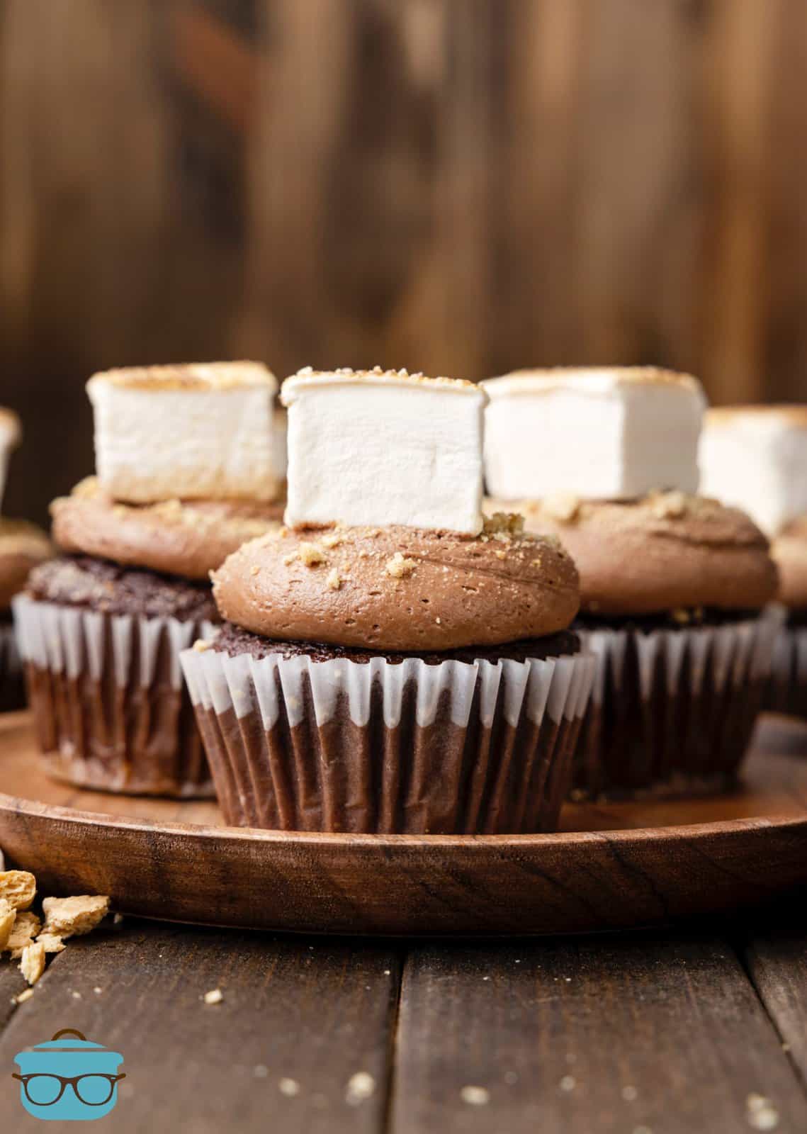 Lined up S'mores Cupcakes on wooden board showing frosting and marshmallow.
