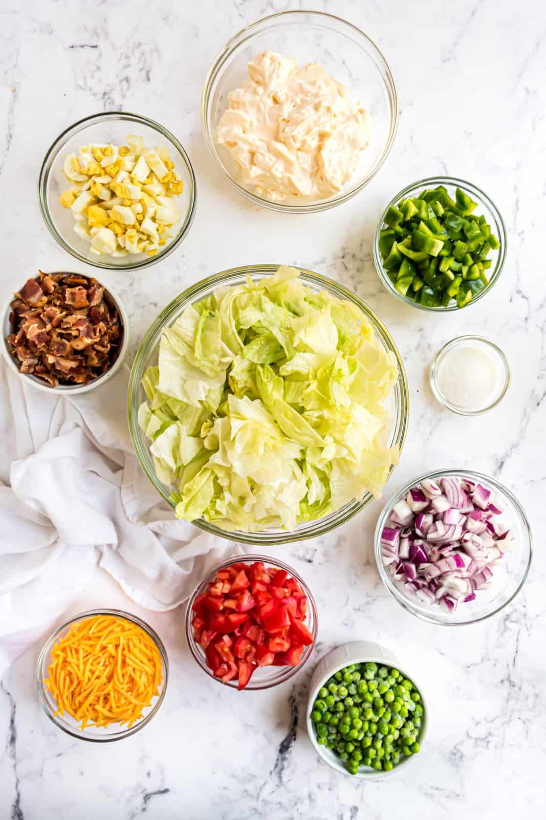 Ingredients needed: head iceberg lettuce, red onion, green pepper, hard-boiled eggs, roma tomatoes, frozen peas, shredded cheddar cheese, bacon, mayonnaise and granulated sugar.