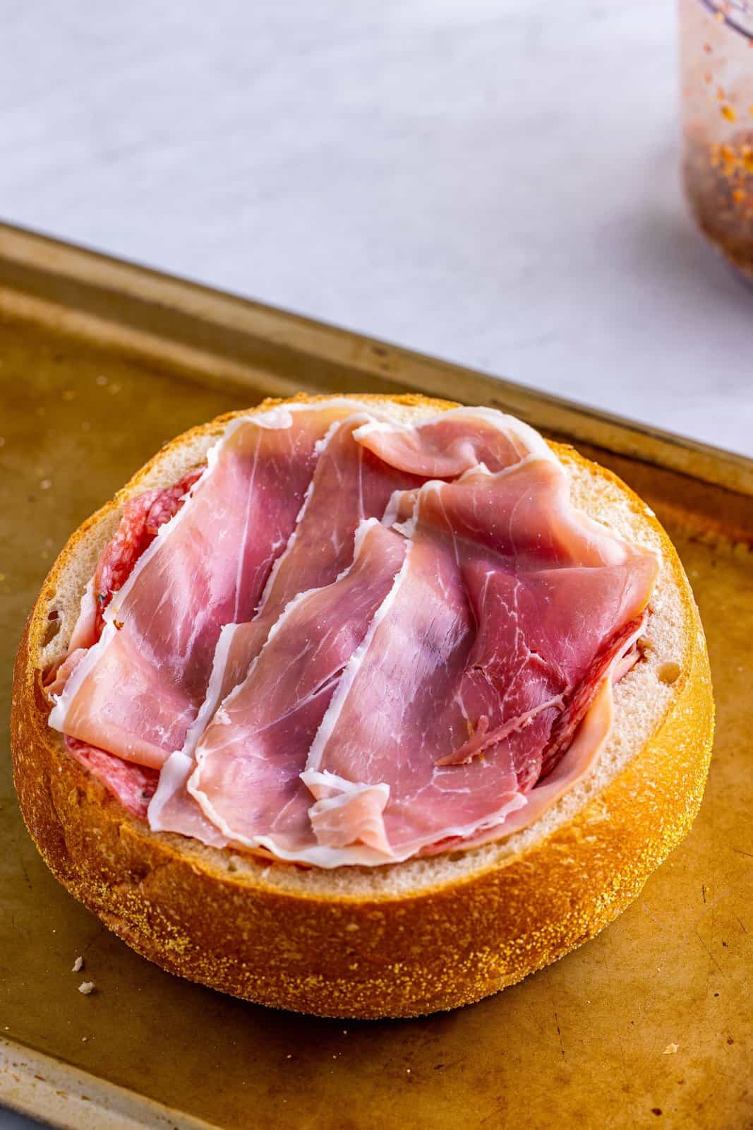 Ham, salami, and prosciutto layered over the cheese and olive spread in bread.