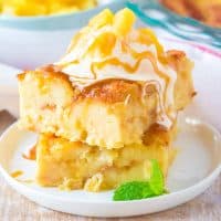 Square image of two slices of Pineapple Bread Pudding stacked on top of one another with toppings on white plate.