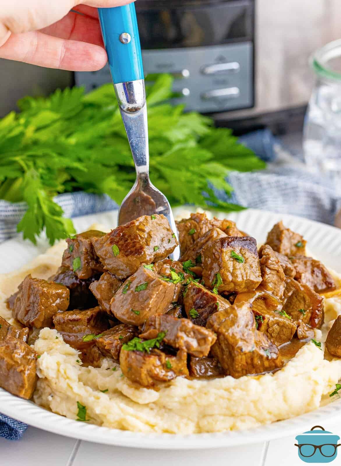 Slow Cooker Garlic Butter Steak Bites over mashed potatoes with fork going into steak.
