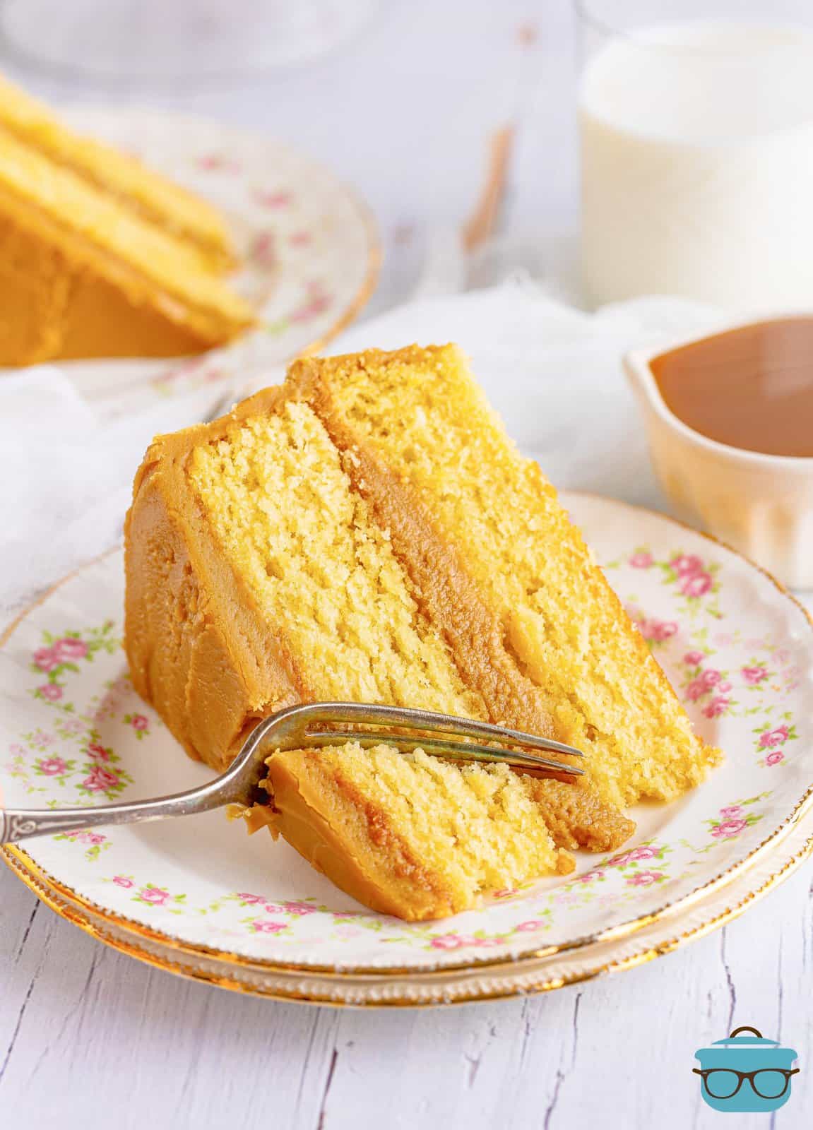 Slice of Southern Caramel Cake on white plate with fork cutting a bite out.