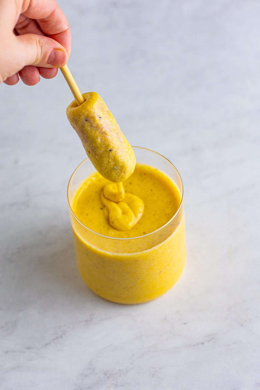 Corn dog dipped into batter in cup.