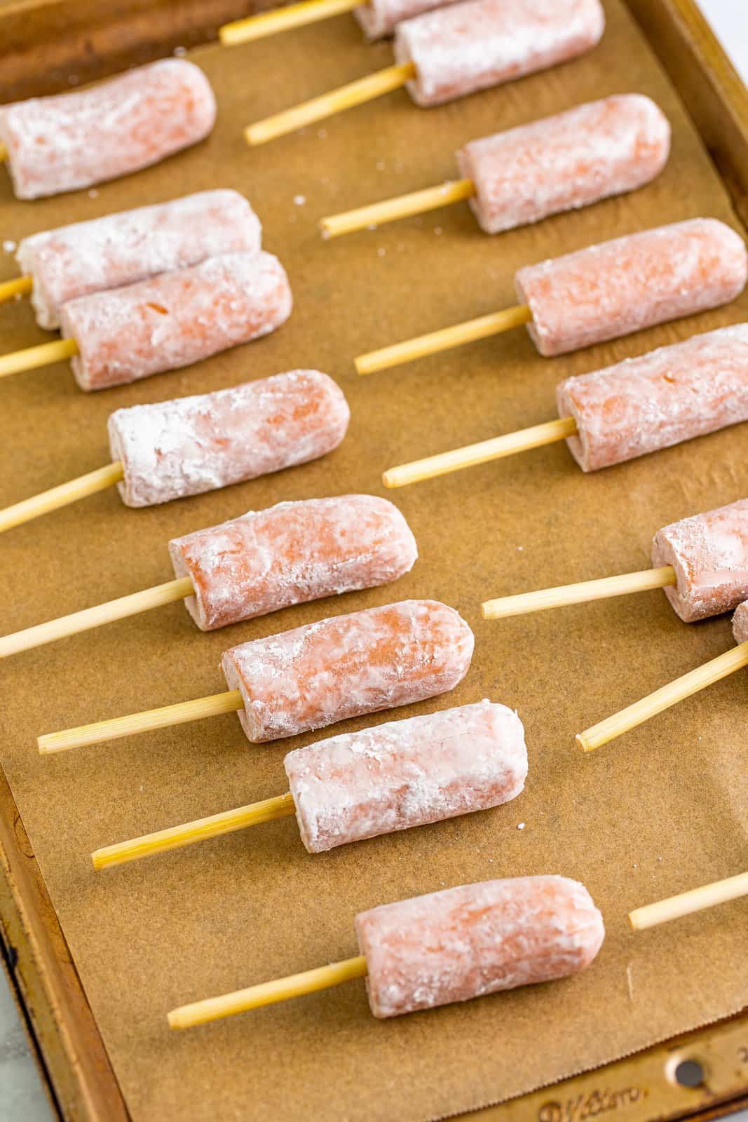Skewers inserted into hot dogs on parchment lined sheet tray.
