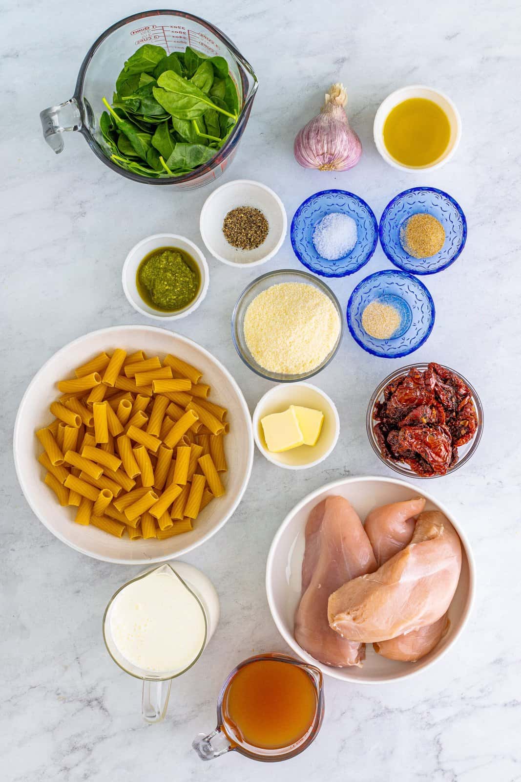 Ingredients needed: boneless skinless chicken breasts, kosher salt, pepper, garlic powder, onion powder, olive oil, salted butter, canned sun-dried tomatoes, garlic, prepared pesto, unsalted chicken stock, heavy cream, baby spinach, parmesan cheese and rigatoni or other short pasta.