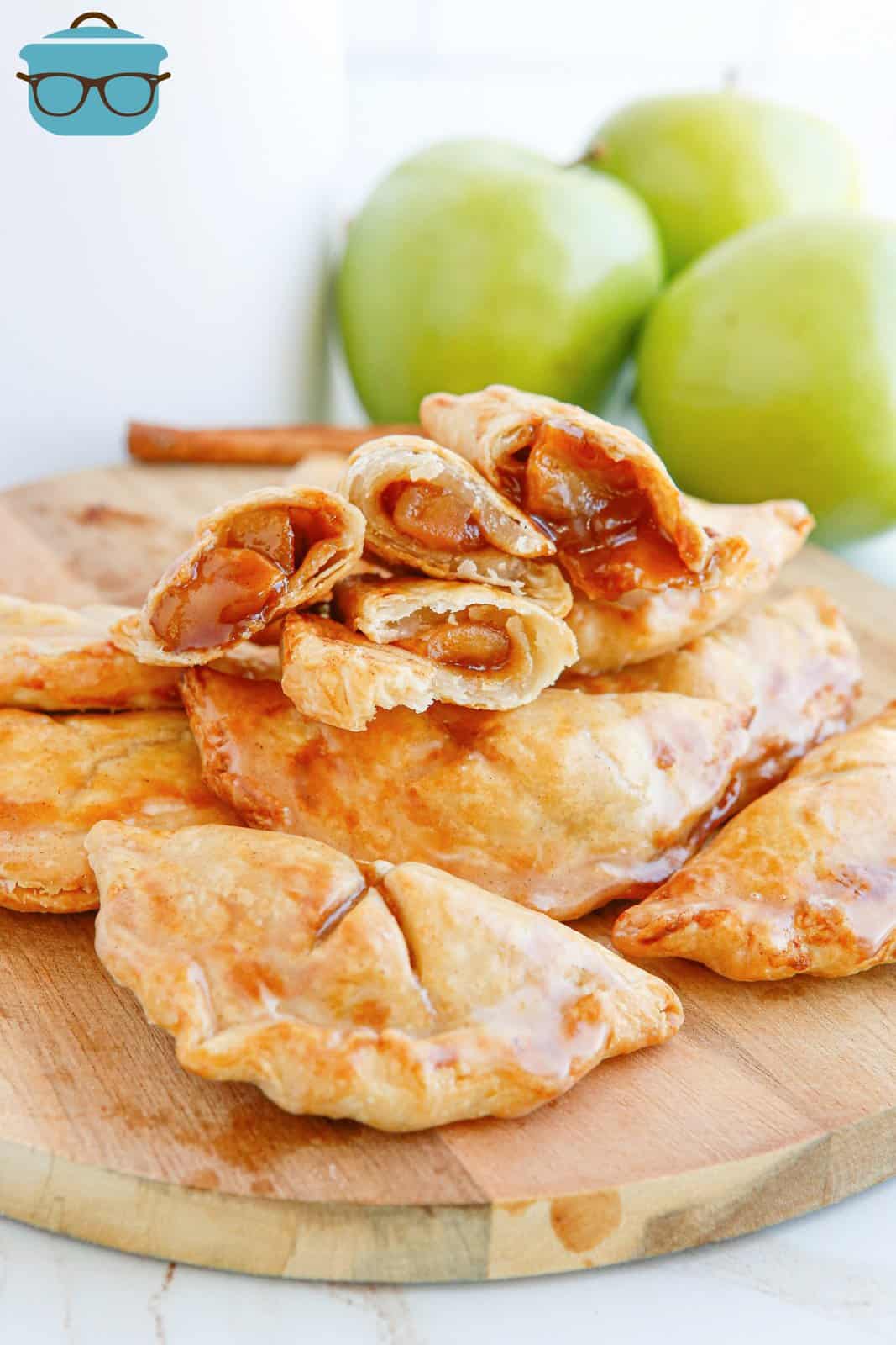 Air Fryer Apple Hand Pies stacked on wooden board with some hand pies split open showing inside.