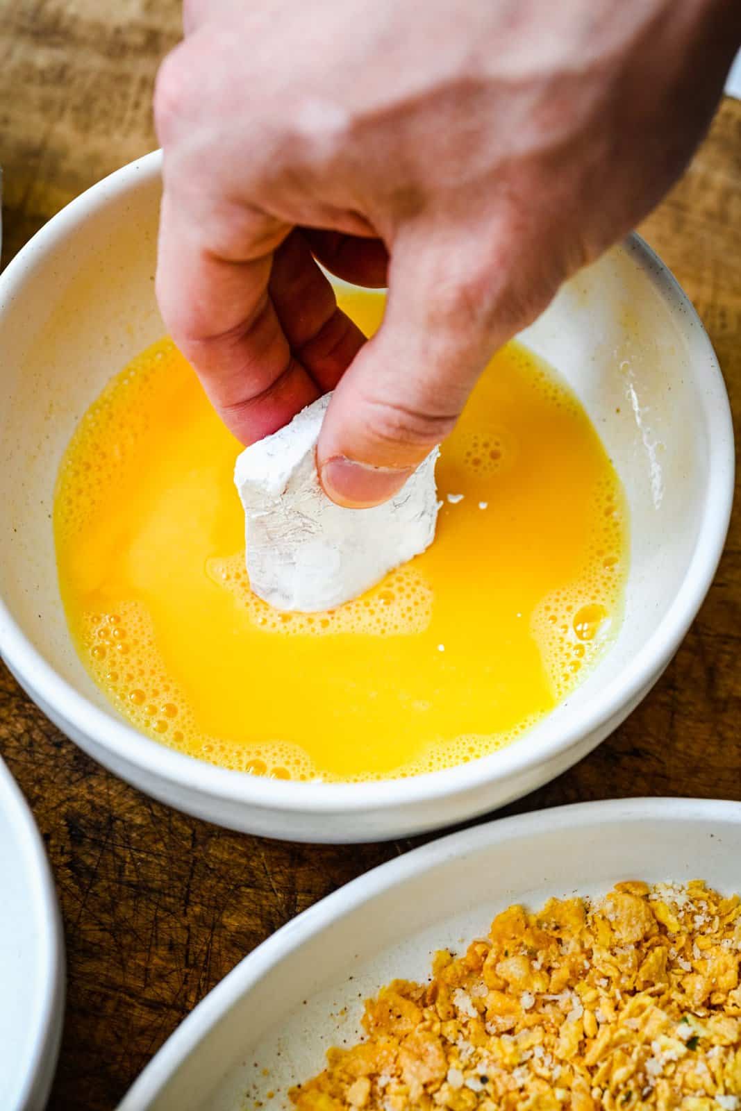 Cornstarch coated chicken piece being dipped in egg.