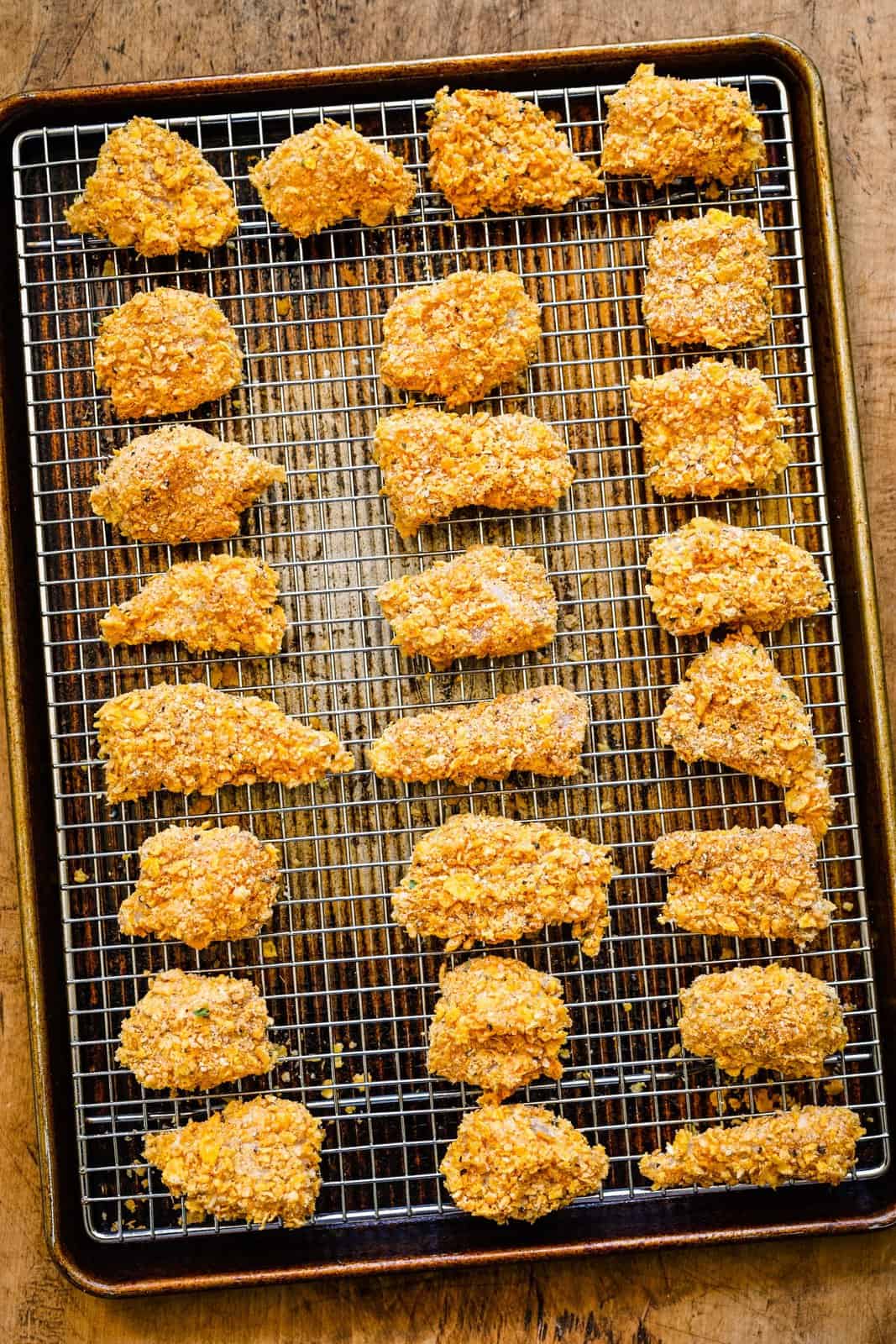 Coated chicken pieces placed on a wire rack over baking pan.