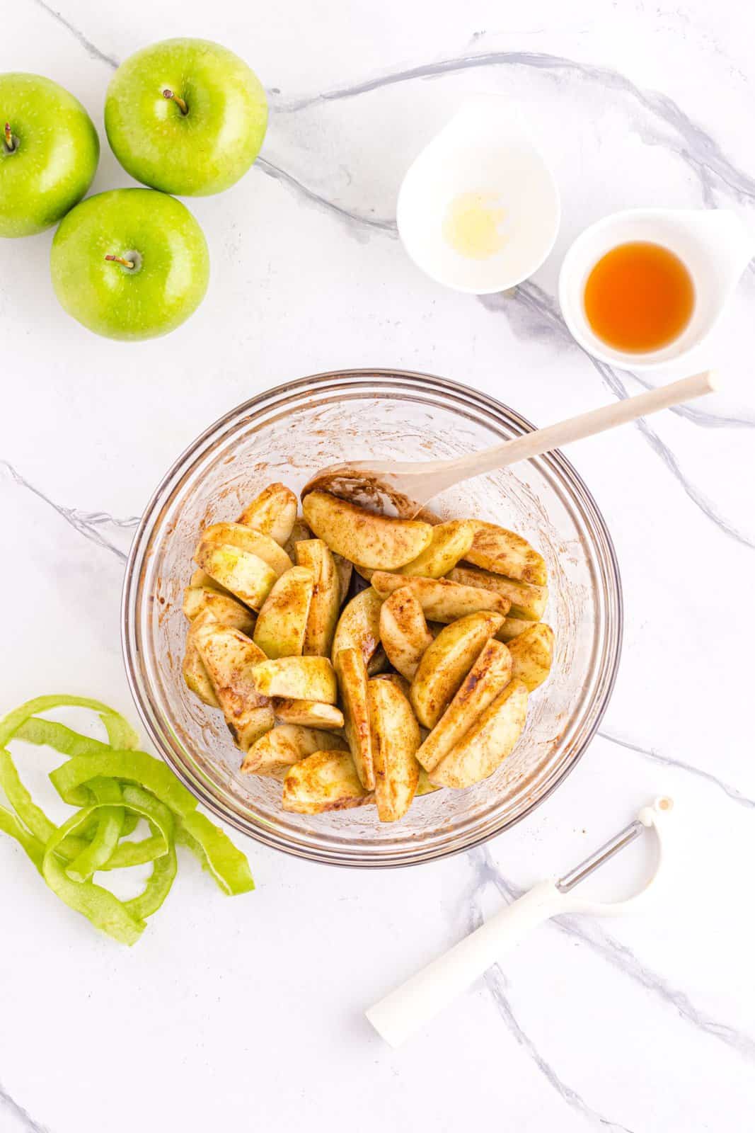 Apples in bowl mixed together with brown sugar, cinnamon, salt, maple syrup and butter.