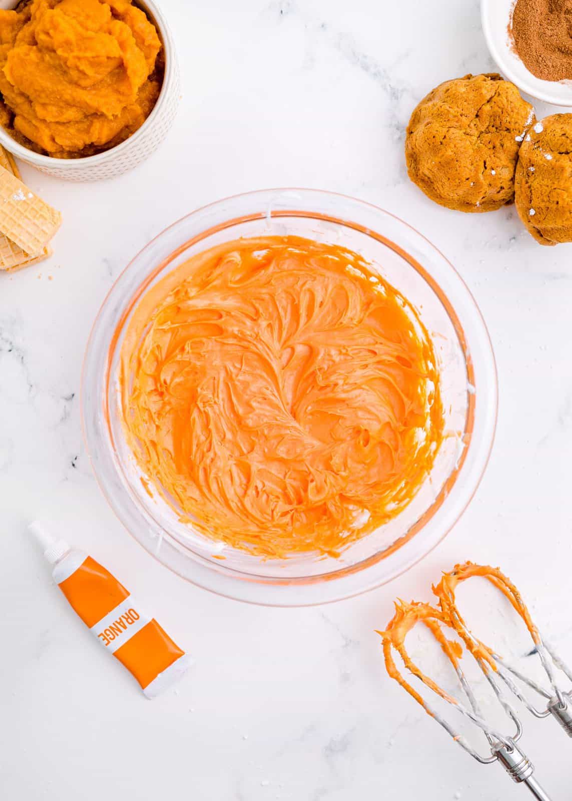 Cream cheese frosting in bowl with orange food coloring.