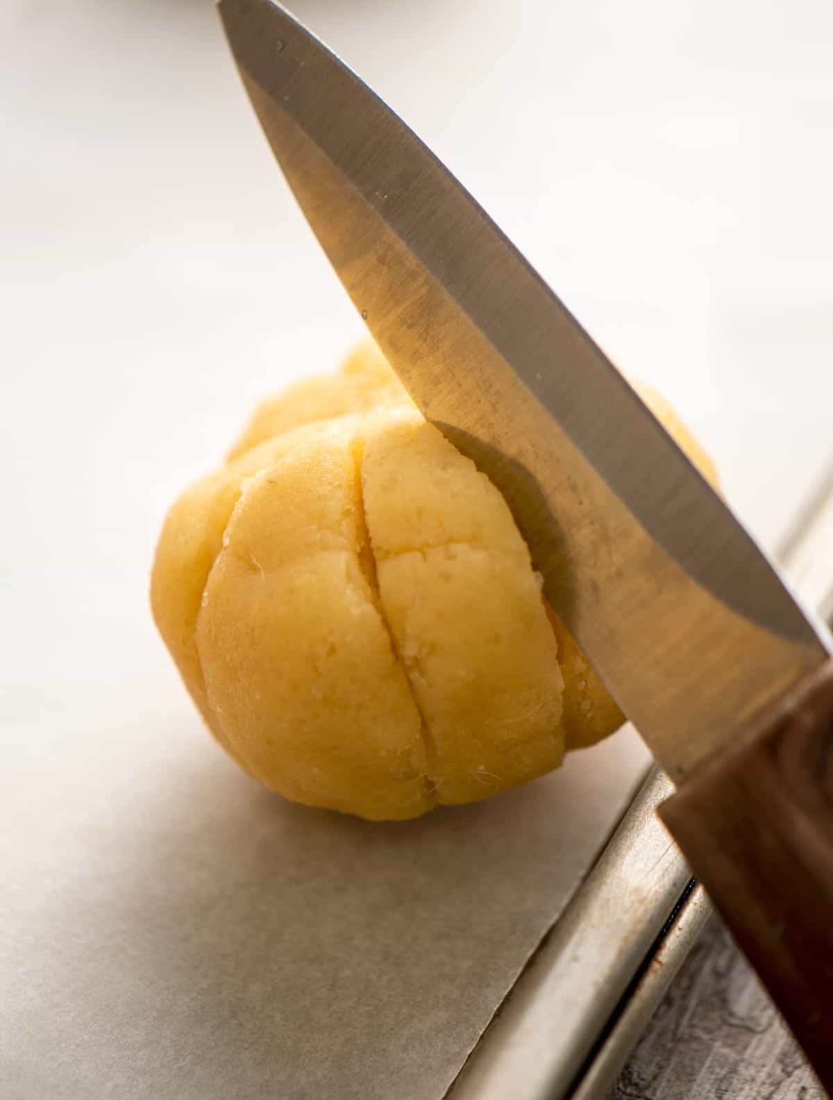 Knife cutting slits into dough balls to shape like pumpkins.