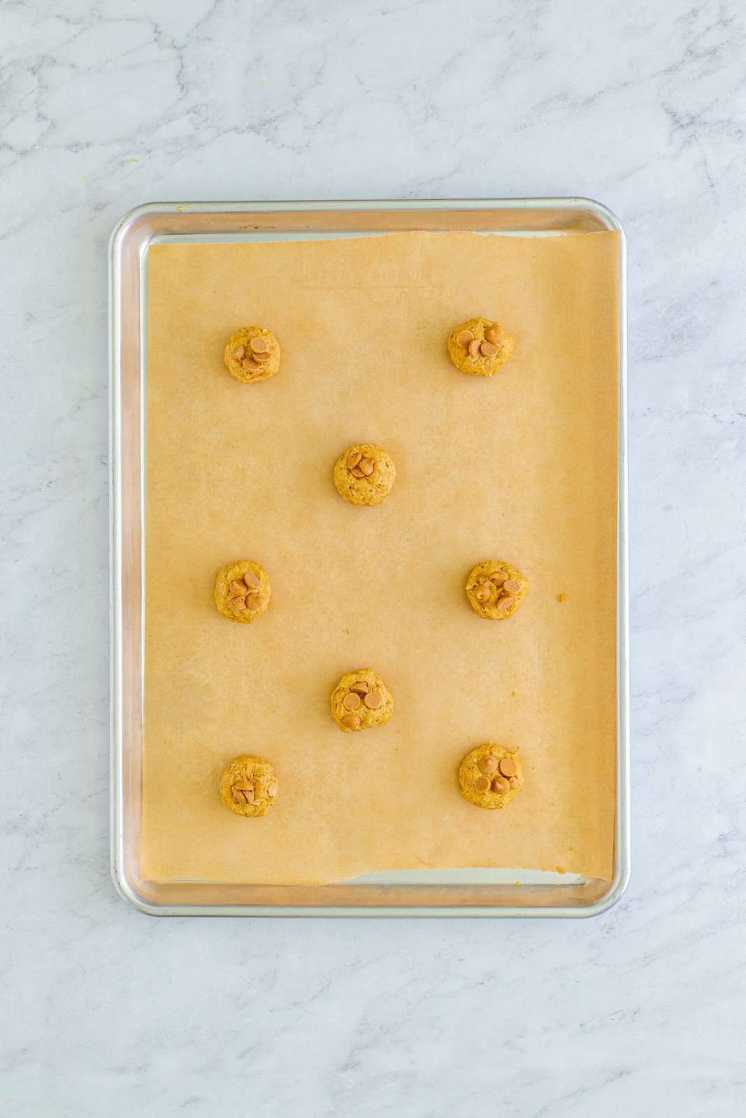 Dough balls with peanut butter chips on parchment lined baking sheet.