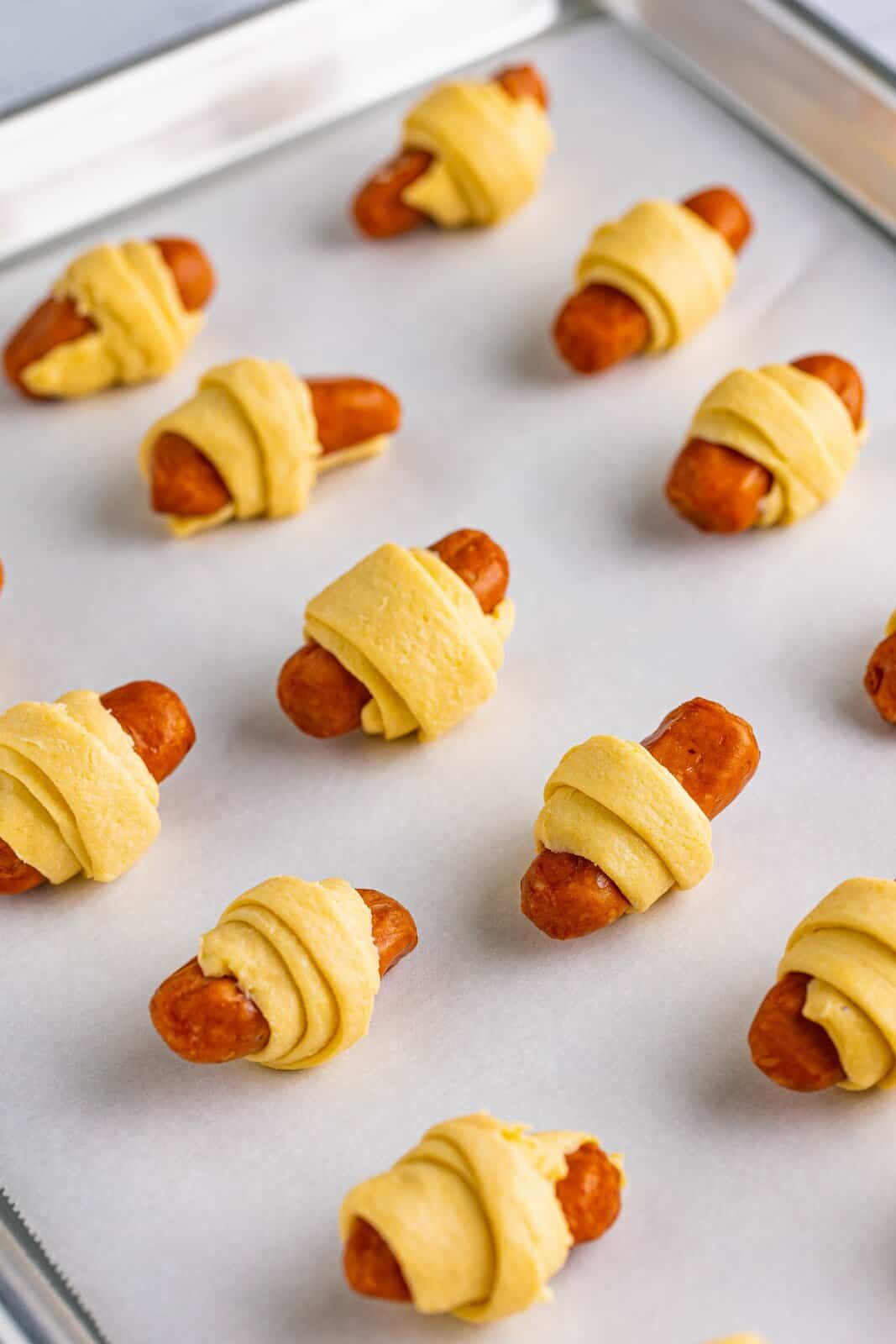 Lil smokies wrapped in crescent rolls on parchment lined baking sheet.