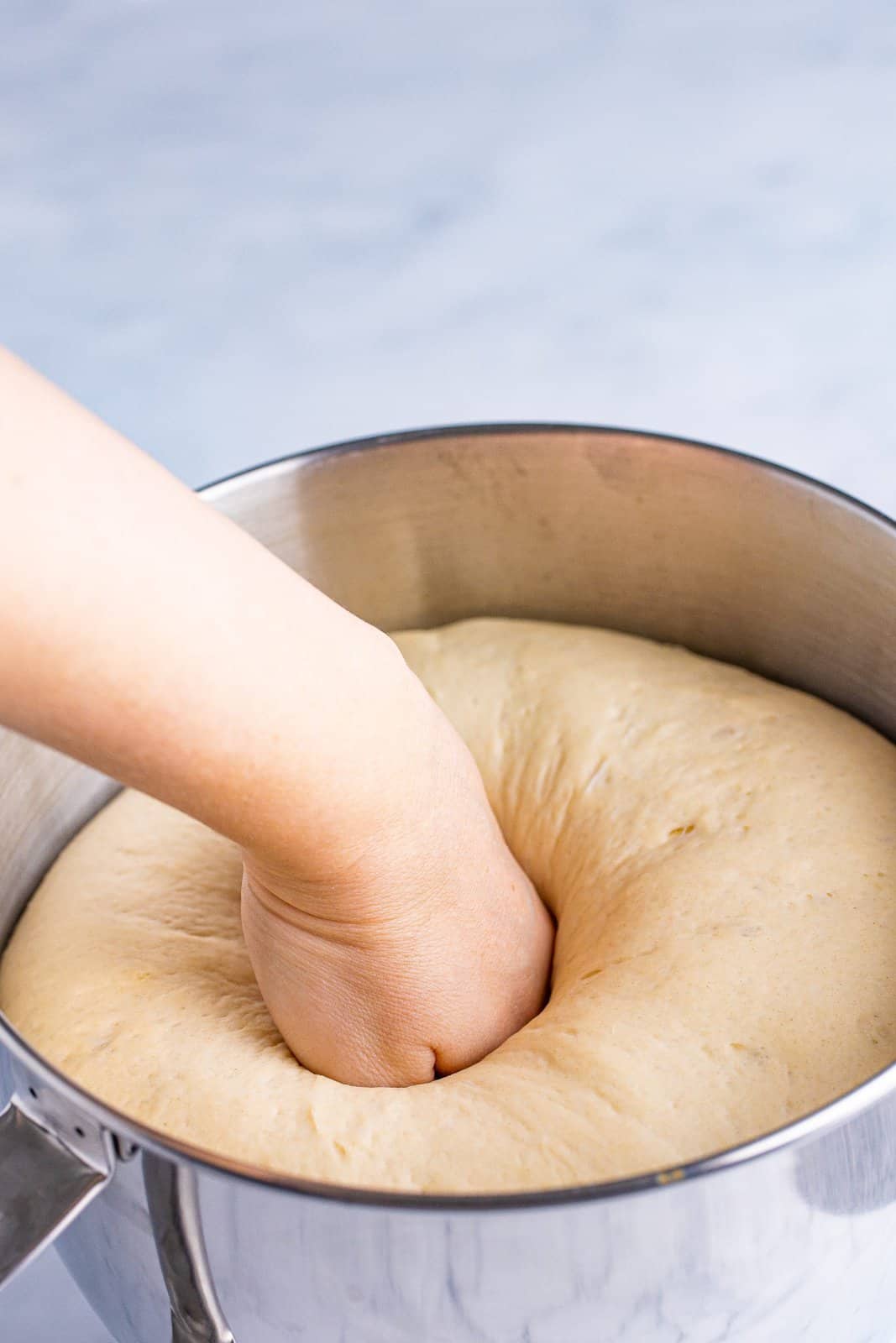 Hand punching down risen dough in bowl of stand mixer.