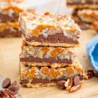 Square image of three stacked Turtle Magic Bars with chocolate chips and nuts.