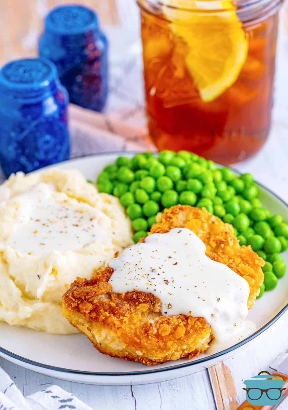 Country Fried Pork Chops and Gravy on plate with mashed potatoes and peas.