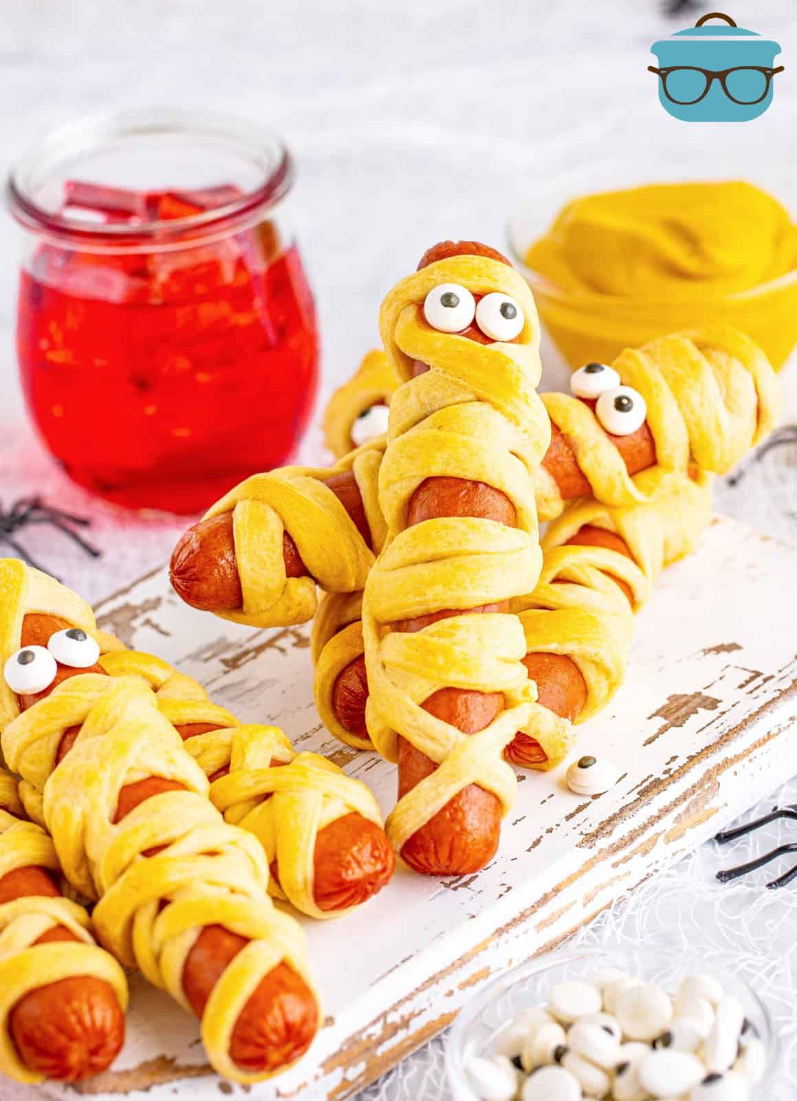 Halloween Mummy Dogs on white wooden board with ketchup in background.