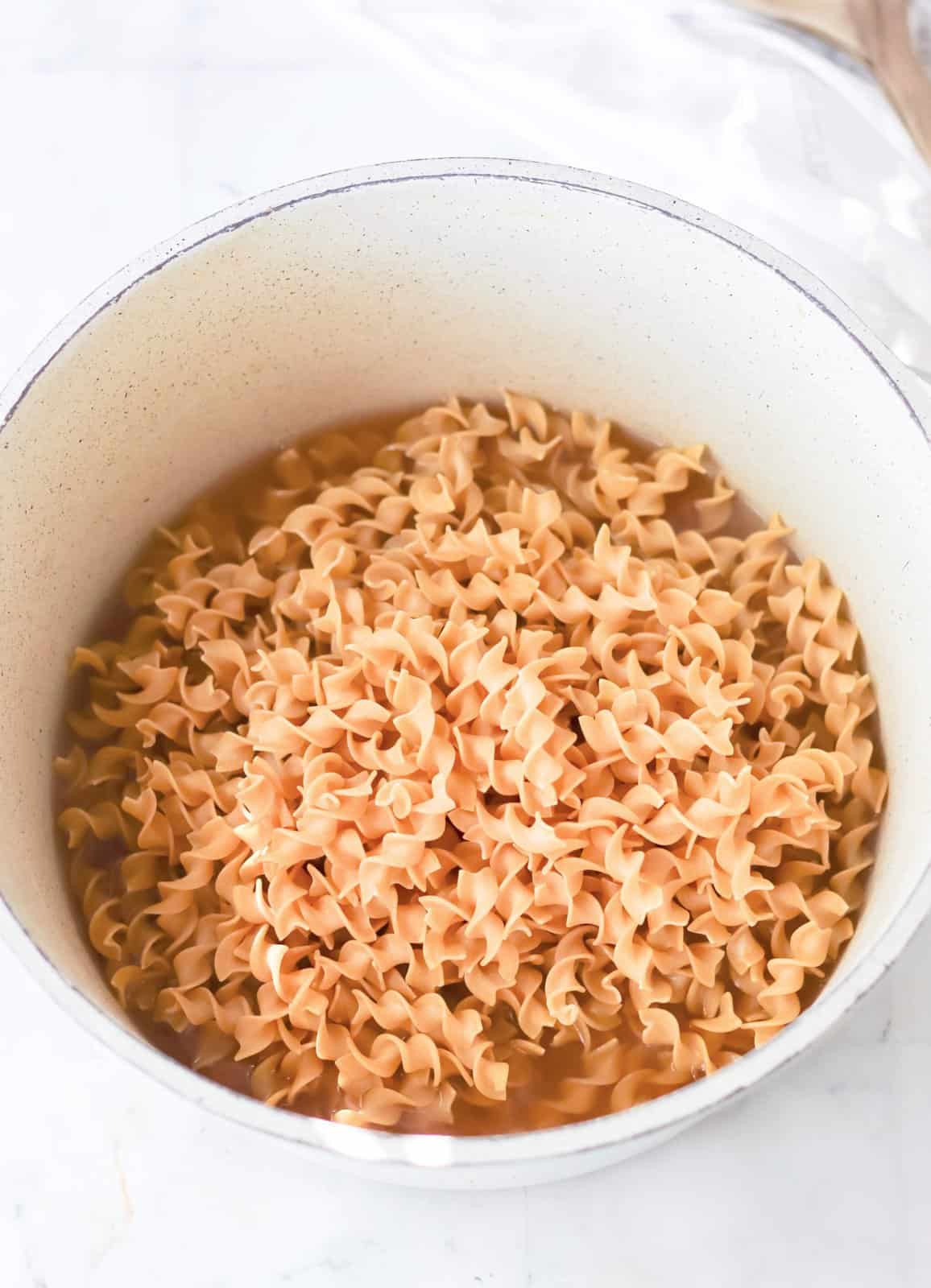Noodles and chicken stock in pan.