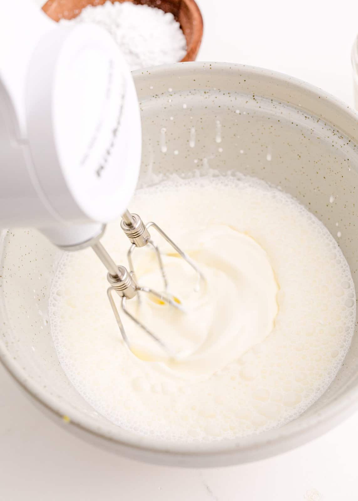 Hand mixer beating the heavy whipping cream in bowl.