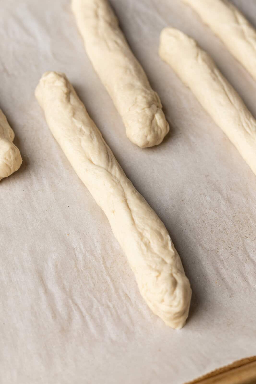 Dough rolled out into long breadsticks on parchment lined baking sheet.