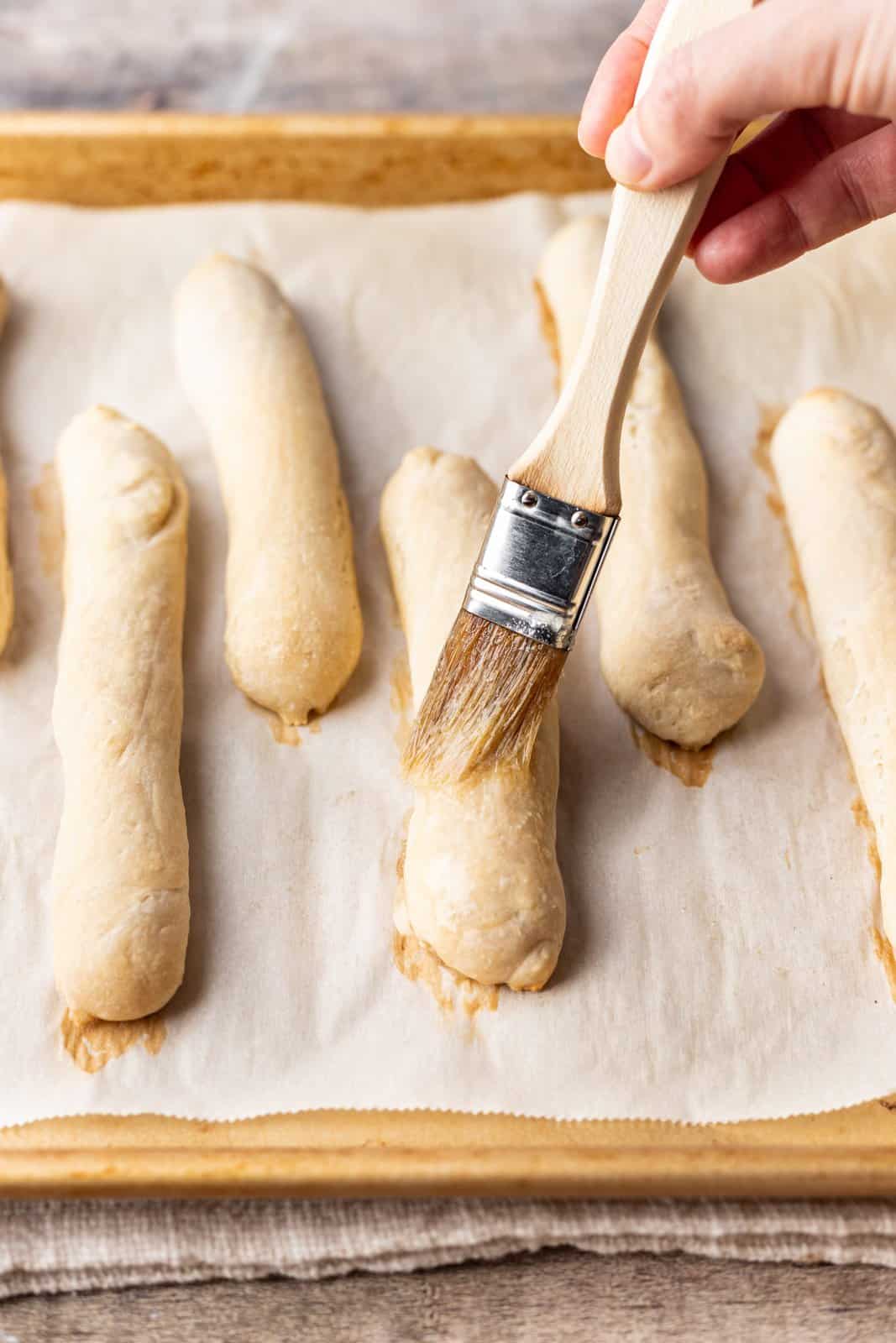 Breadsticks being brushed with a butter and garlic powder mixture.